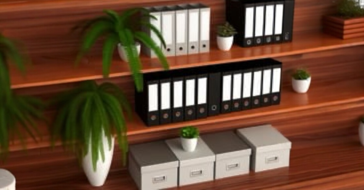 there are items arranged neatly on the shelf. There are white binders and black binders. There are also boxes that probably contain photos. There are plants with white bases, arranged among the binders in boxes. The shelf is brown.